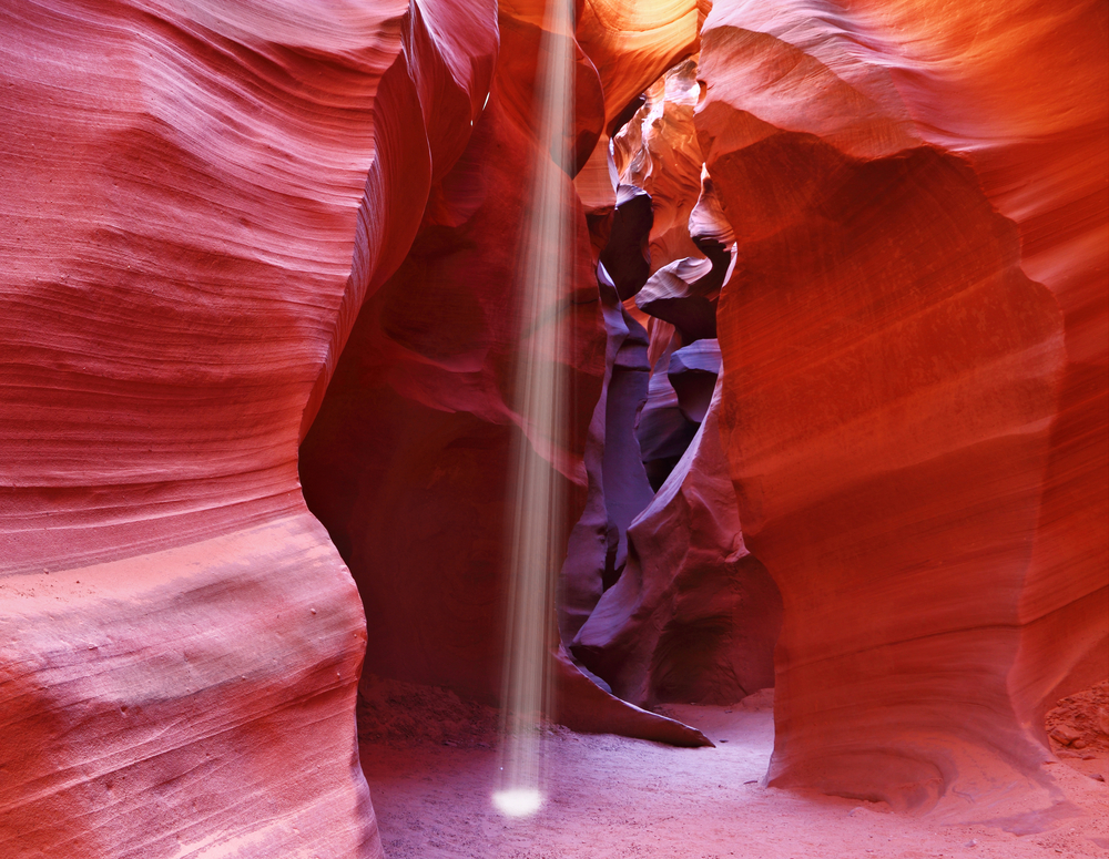 A thin ray of sunlight illuminates the sandy bottom of the canyon