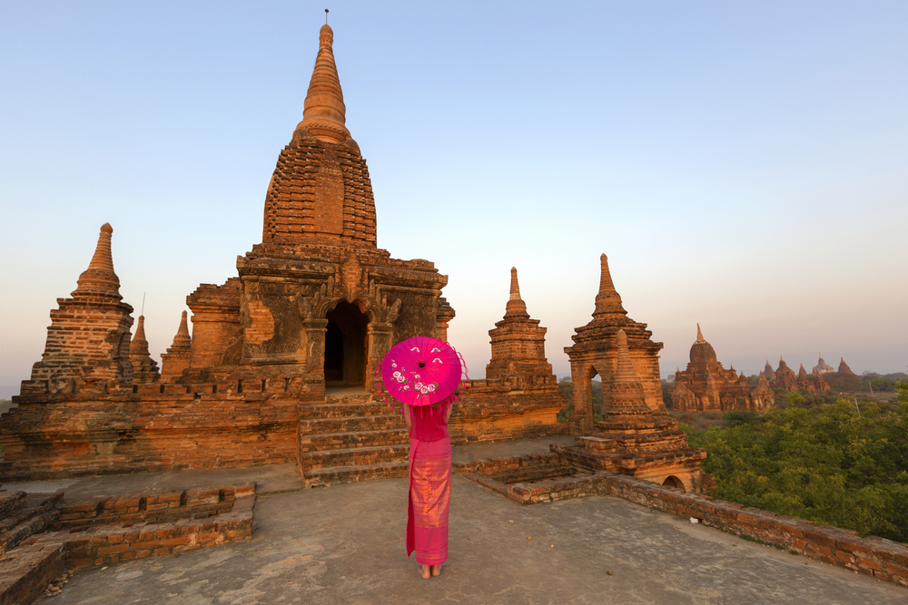 Law Ka Ou Shaung temple with a traditionally dressed lady with umbrella in front Bagan Myanmar 
